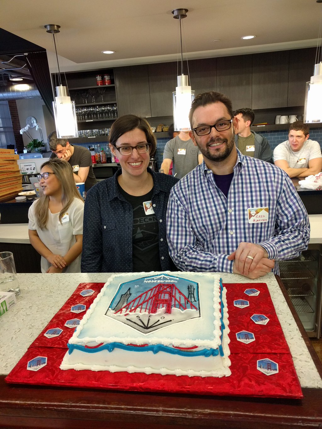 a picture of myself with Reza Akhavan and the awesome cake shaped like our sticker logo that we had for the meetup on the 1 year anniversary of NodeSchool SF